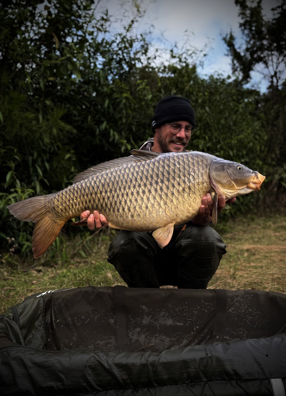 Angler with a big common carp on the unhooking mat