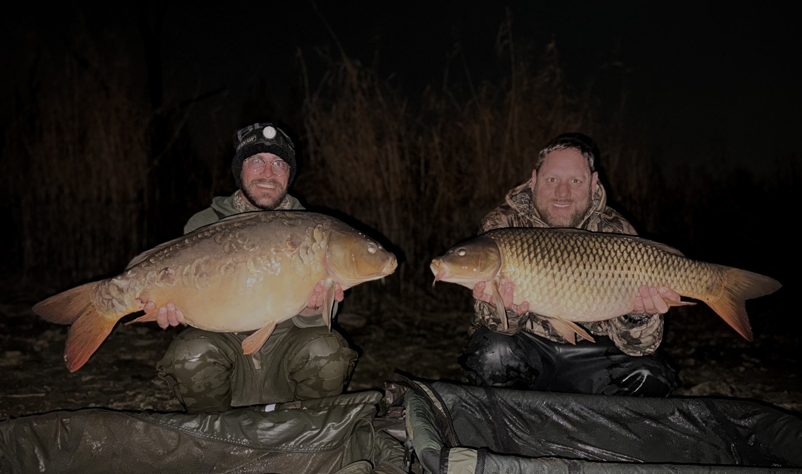 Two anglers at night holding two large common carp