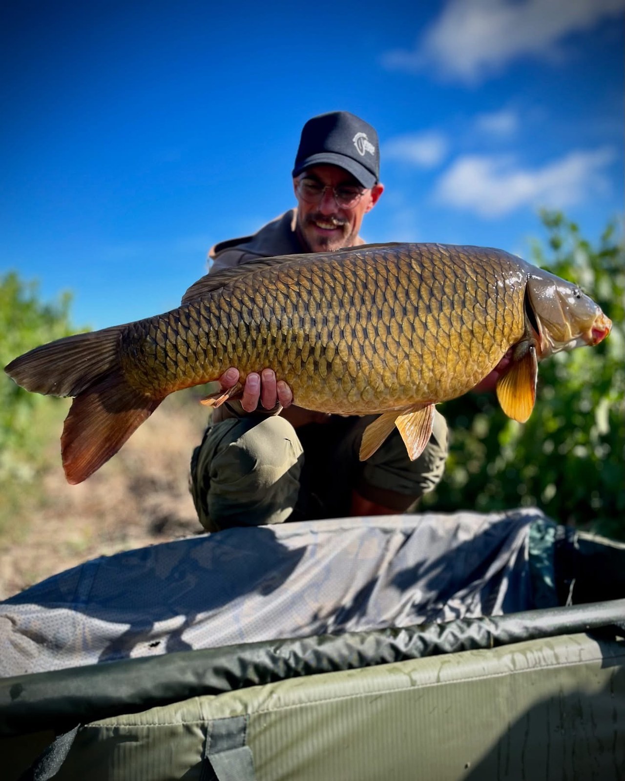 Angler holding a big common carp under a blue sky